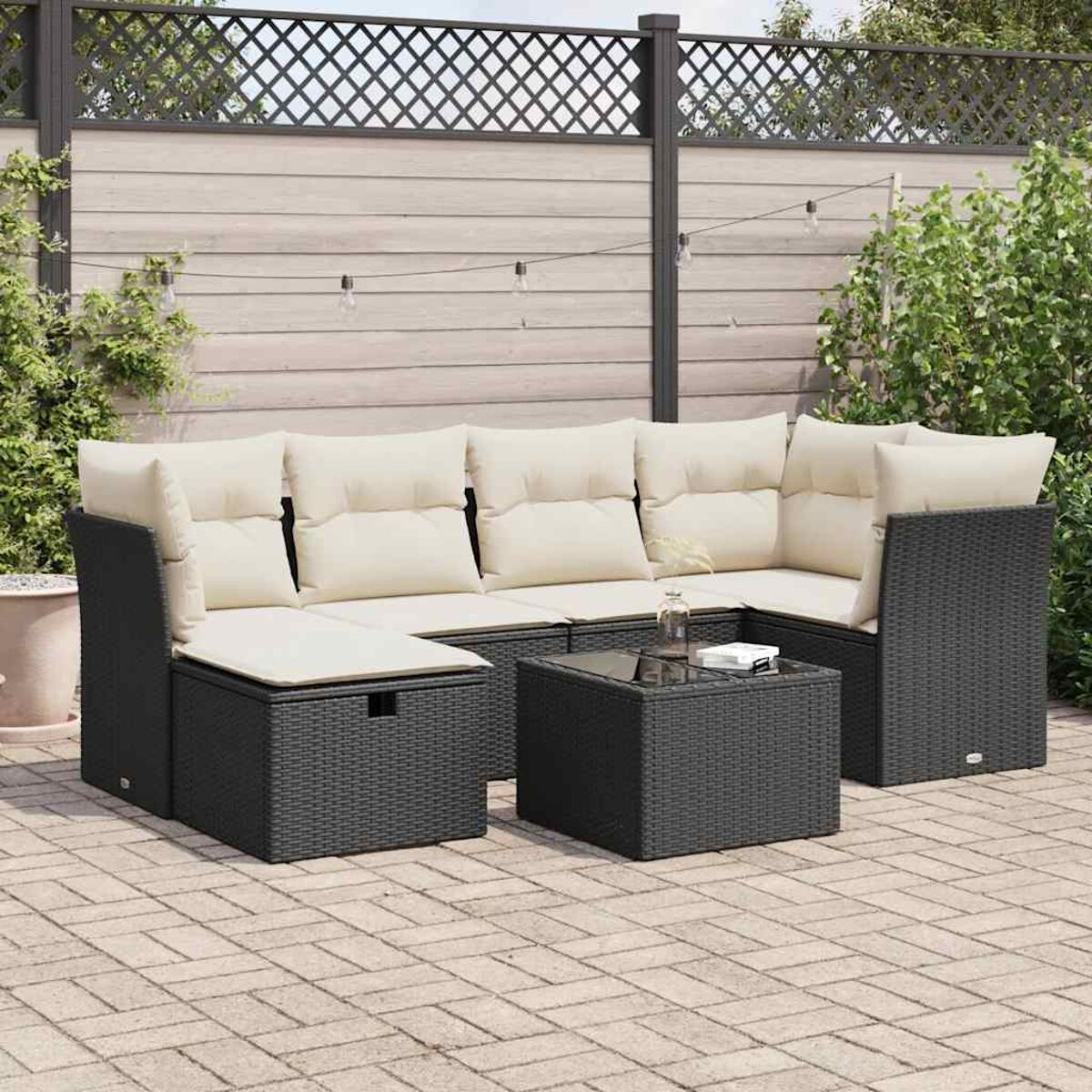 Schwarzes Outdoor-Ecksofa mit cremefarbenen Kissen und einem schwarzen Couchtisch. Gepflasterte Terrasse.
