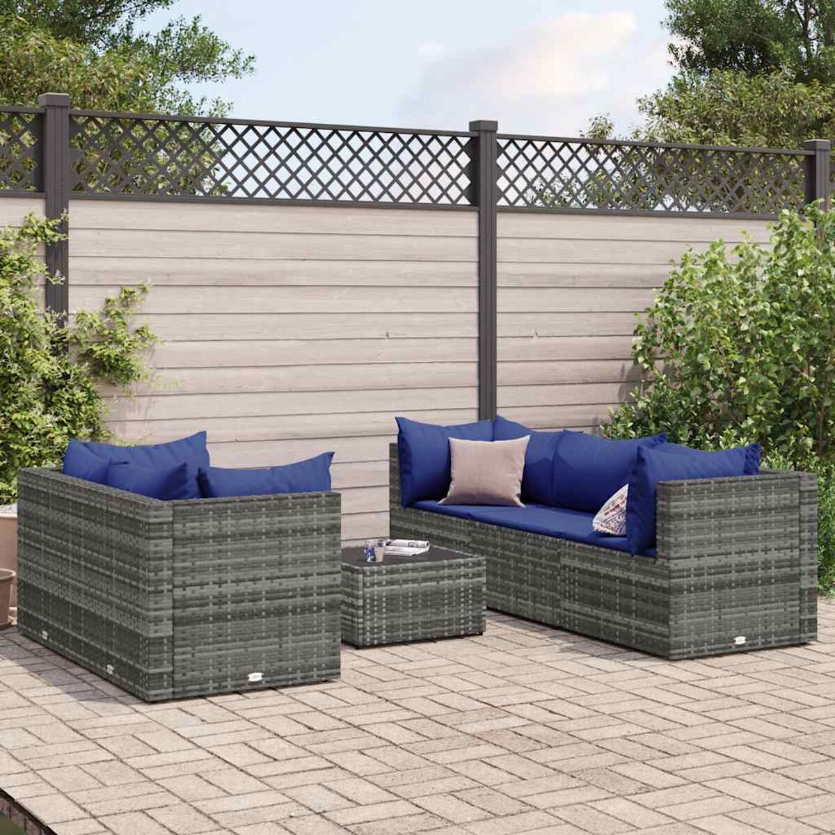 Set di mobili in vimini grigi per esterni su un patio in mattoni. Include divano, sedia e tavolino con cuscini blu.