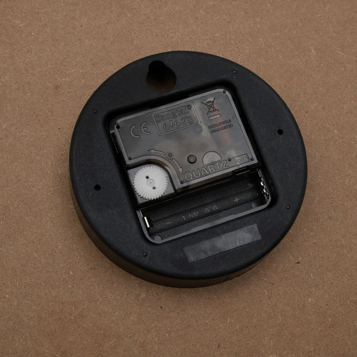 Uhrwerk. Schwarz, kreisförmig mit Quarzdetails, Batteriefach, Zahnrädern und einem 'Sangtai'-Etikett.
