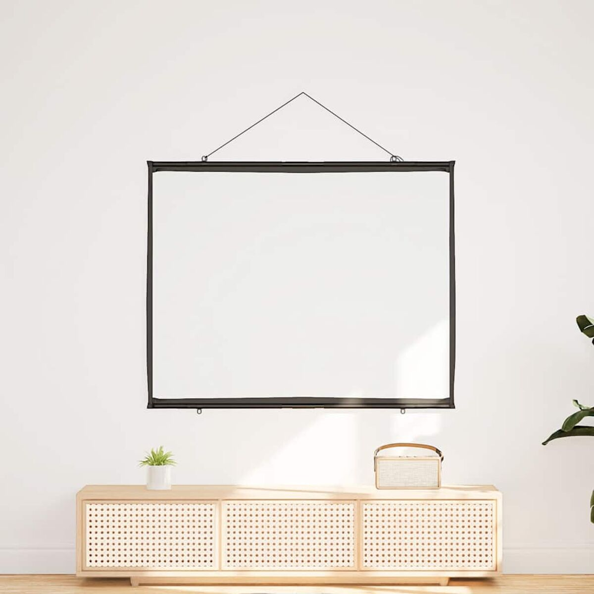 Eine weiße Projektionsleinwand hängt an einer weißen Wand. Darunter sind ein Holzschrank und eine Pflanze zu sehen.