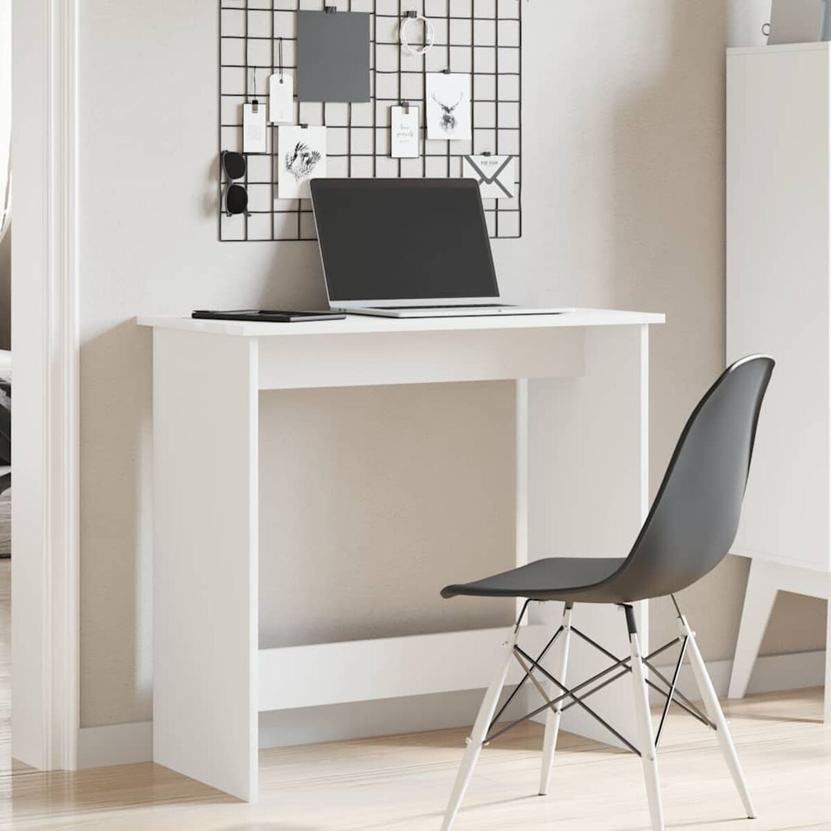 Weißer Schreibtisch mit Laptop und schwarzem Stuhl. Hintergrund ist ein Gitter und Dekorationen.