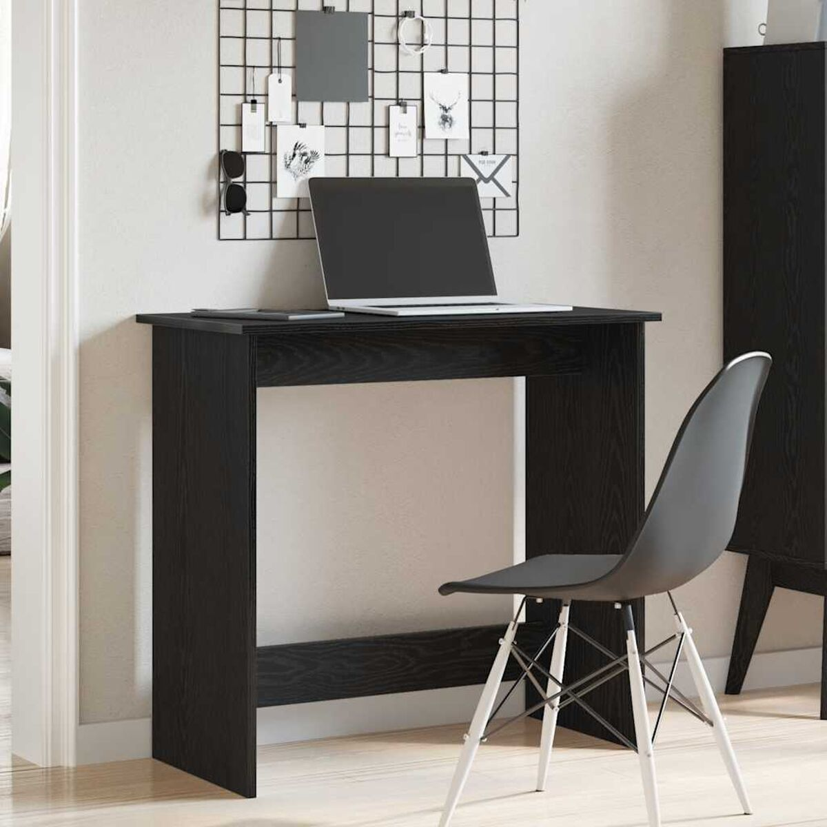 Schwarzer Schreibtisch mit Laptop, Stuhl und Gitter an der Wand.