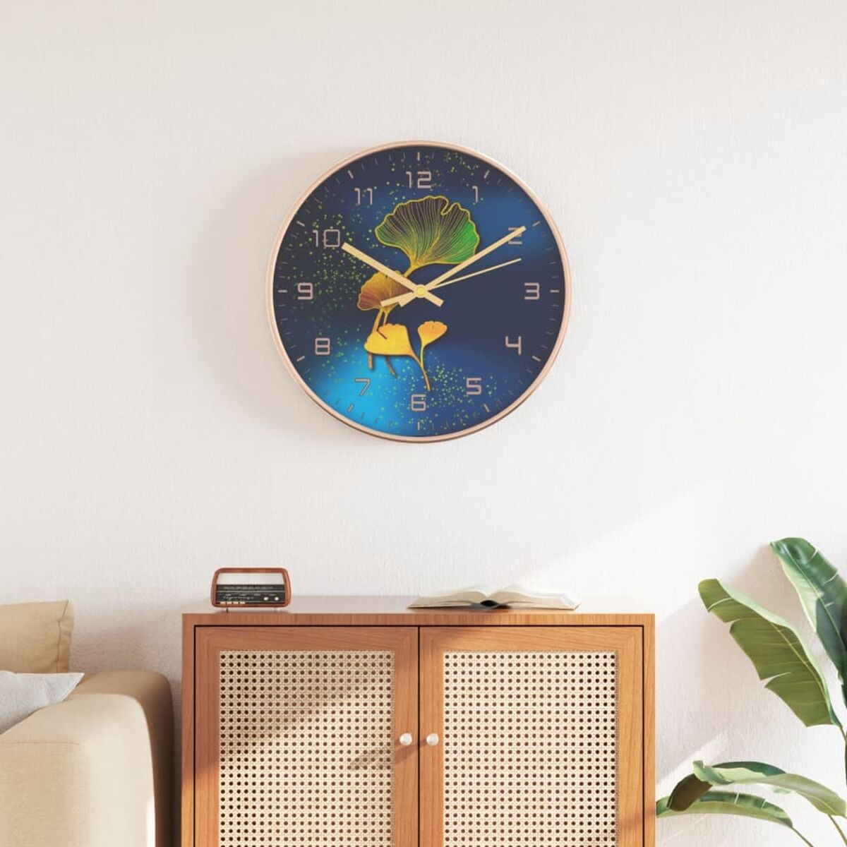 Runde Wanduhr mit goldenem Rahmen, blauem Zifferblatt und Ginkgo-Blatt-Design. Schrank darunter.