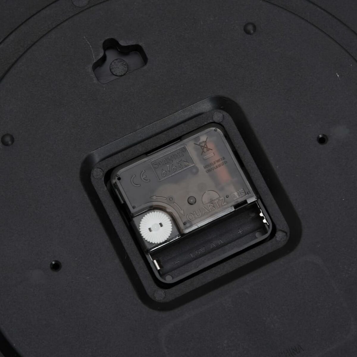 Die Rückseite eines schwarzen Uhrwerks. Zwei Batterien und ein Quartz-Etikett sind sichtbar.