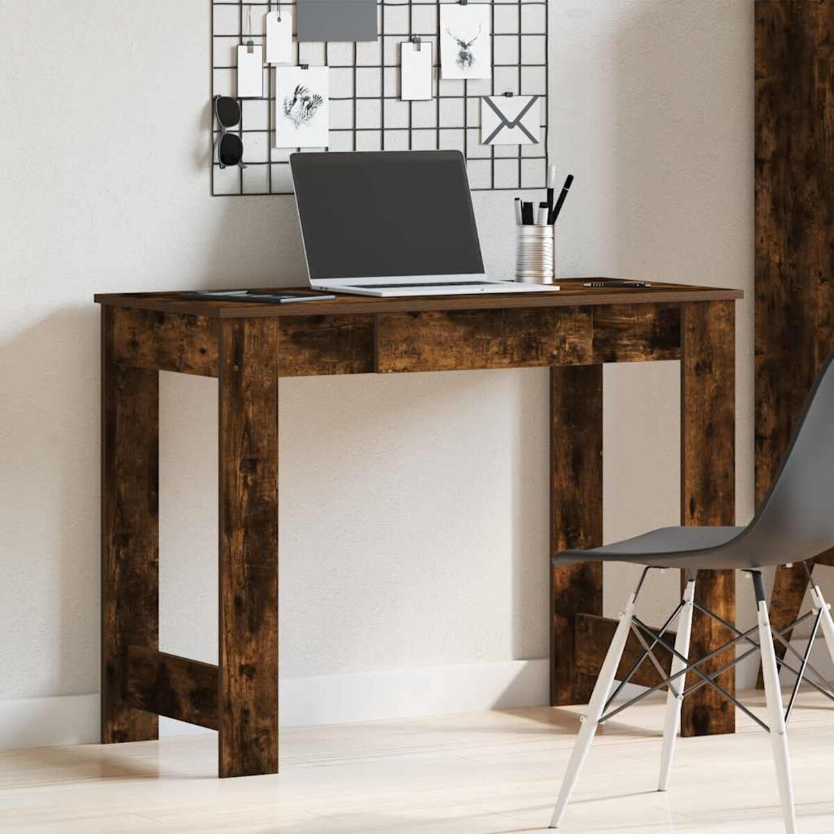 Ein brauner Holzschreibtisch mit Laptop, Stiften und Stuhl vor einer weißen Wand mit Gitter.