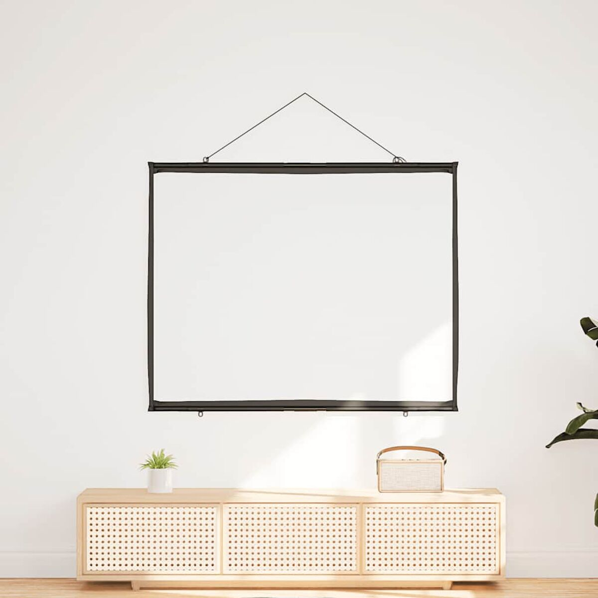 Eine weiße Projektionsleinwand hängt an einer weißen Wand. Darunter sind ein Holzschrank und eine Pflanze zu sehen.