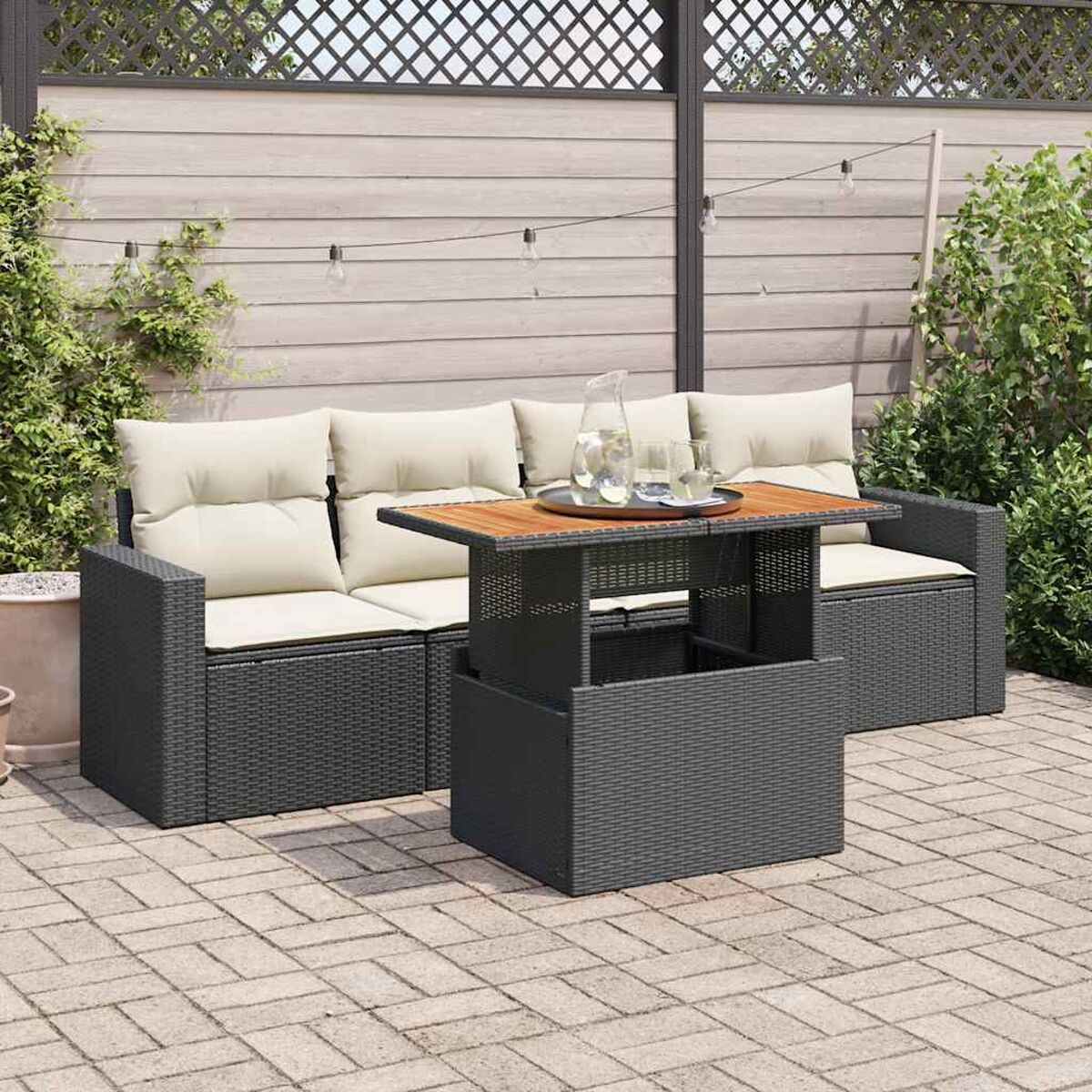 Set patio esterno: divani in rattan grigio, cuscini beige e un tavolo con piano in legno e bicchiere d'acqua.