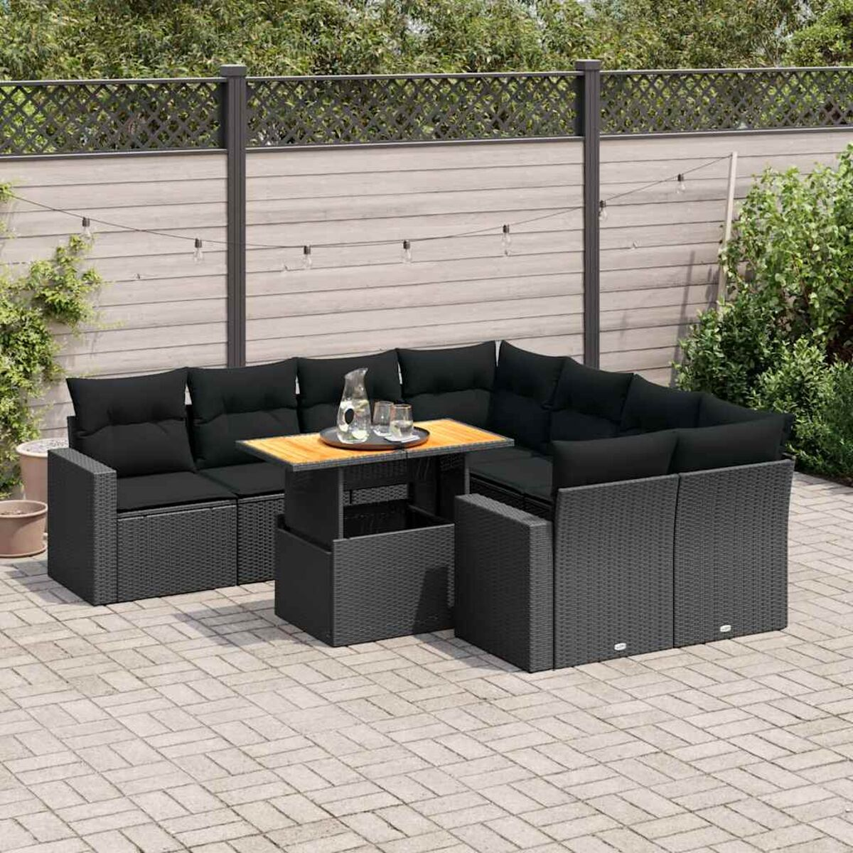 Ein schwarzes Rattan-Outdoor-Sofa-Set mit einem Holztisch und Kissen. Der Hintergrund ist Grün.