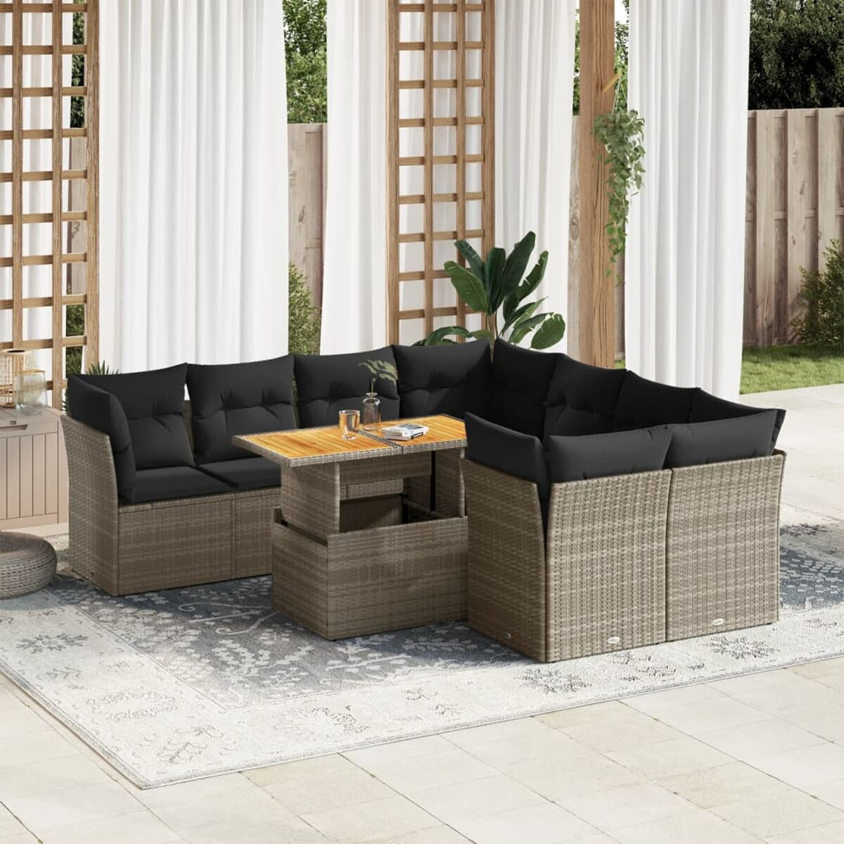Set di mobili da esterno in rattan con tavolo rialzabile, cuscini bianchi e tappeto.