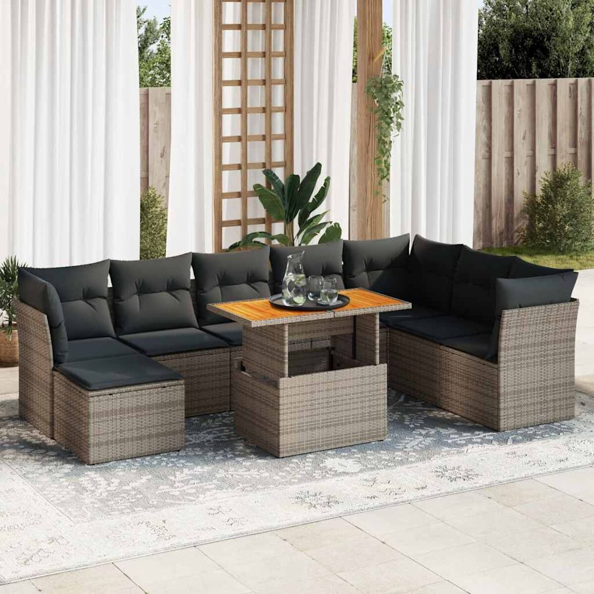 Un set di sedute da esterno in rattan. Ha un divano componibile, un tavolino e un tappeto. La scena è all'aperto.