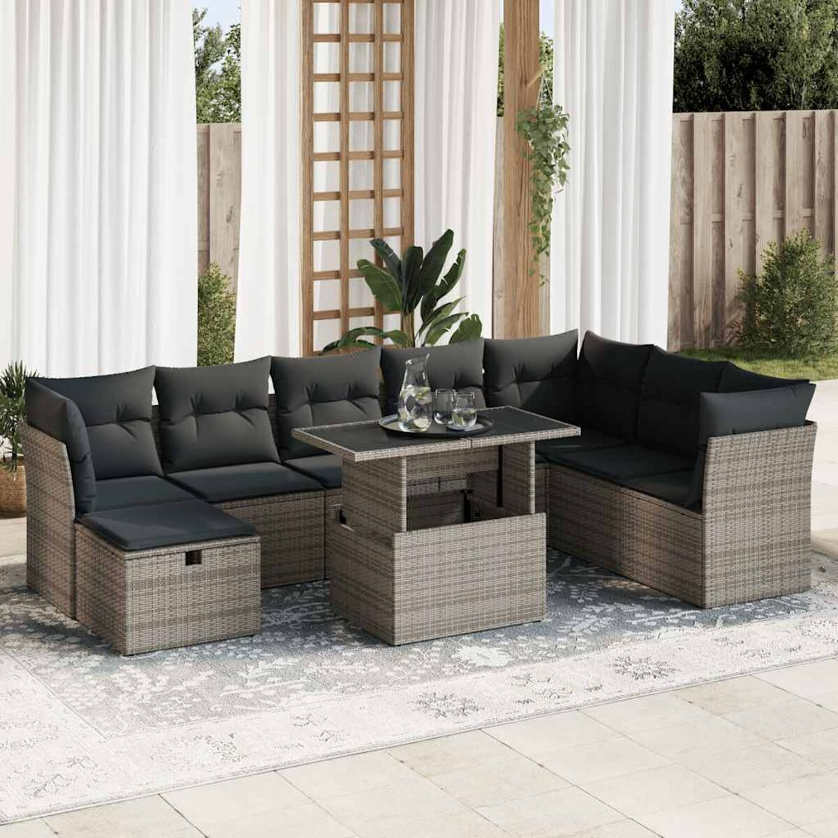 Rattan-Sitzgruppe für draußen mit dunkelgrauen Kissen, Glastisch und Gläsern auf den Tischen.