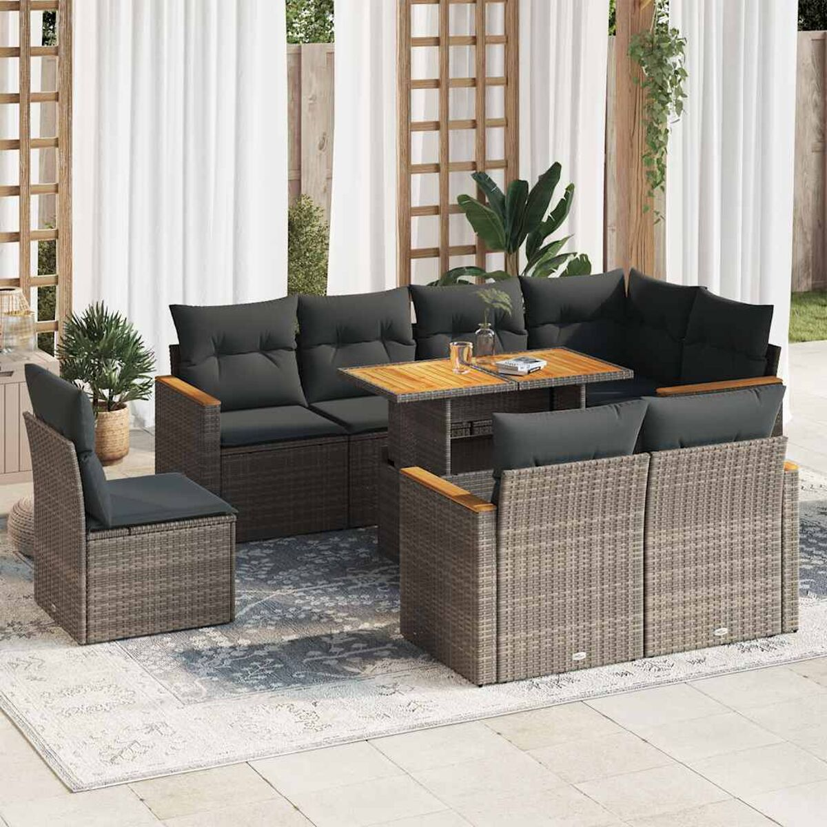 Set divano in rattan da esterno con cuscini grigi e tavolo in legno, su un tappeto.