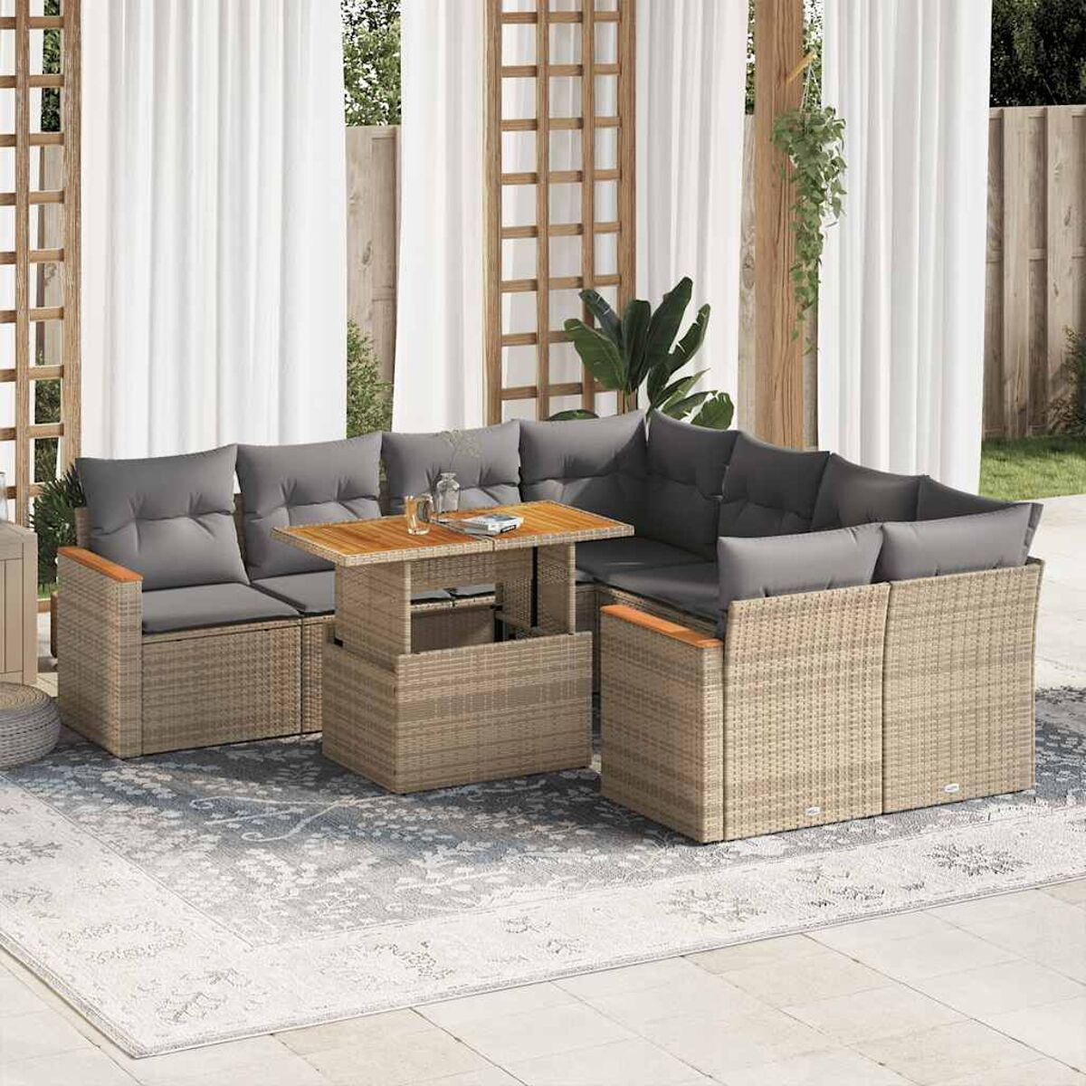 Set di mobili da esterno in rattan con tavolo e cuscini grigi. Tende visibili.