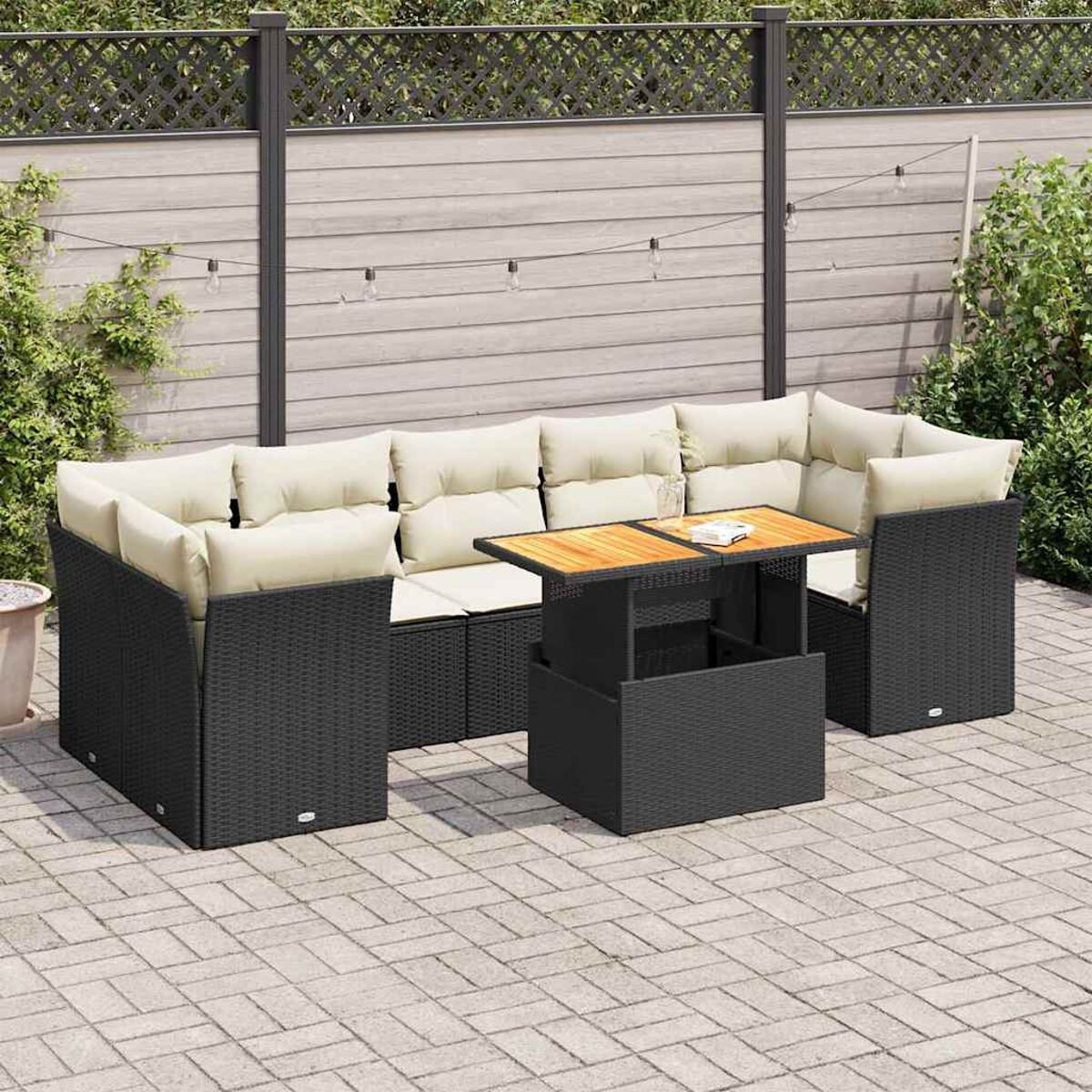Schwarzes, gewebtes Outdoor-Sofa-Set mit beigen Kissen, Tisch, vor Zaun und grünem Hintergrund.