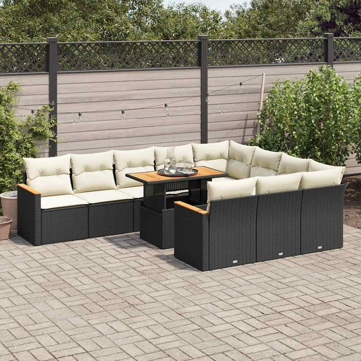 Set di mobili in vimini neri per esterni con cuscini beige, su patio pavimentato.