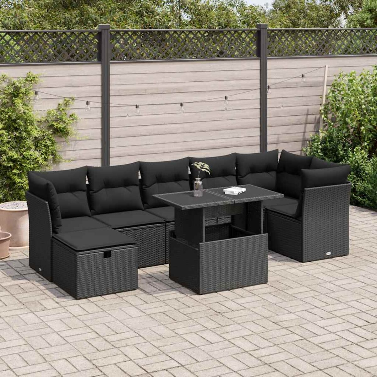 Schwarzes Outdoor-Ecksofa mit Hubtisch auf einer Backstein-Terrasse, Zaun im Hintergrund.