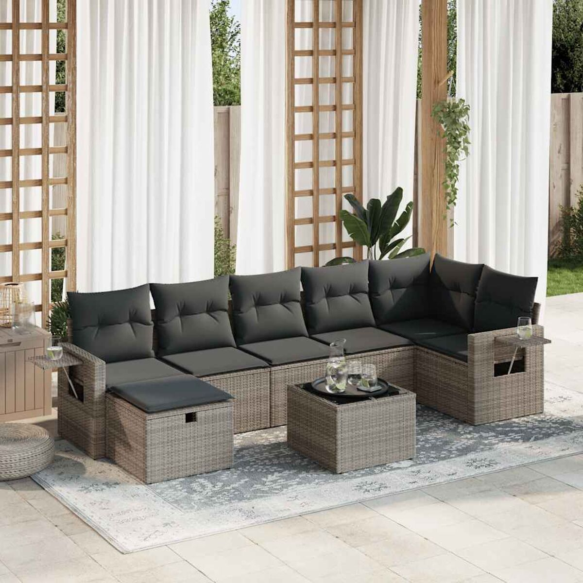 Graues Outdoor-Ecksofa aus Korbgeflecht mit Kissen, einem Tisch mit Getränken und weißen Vorhängen im Hintergrund.
