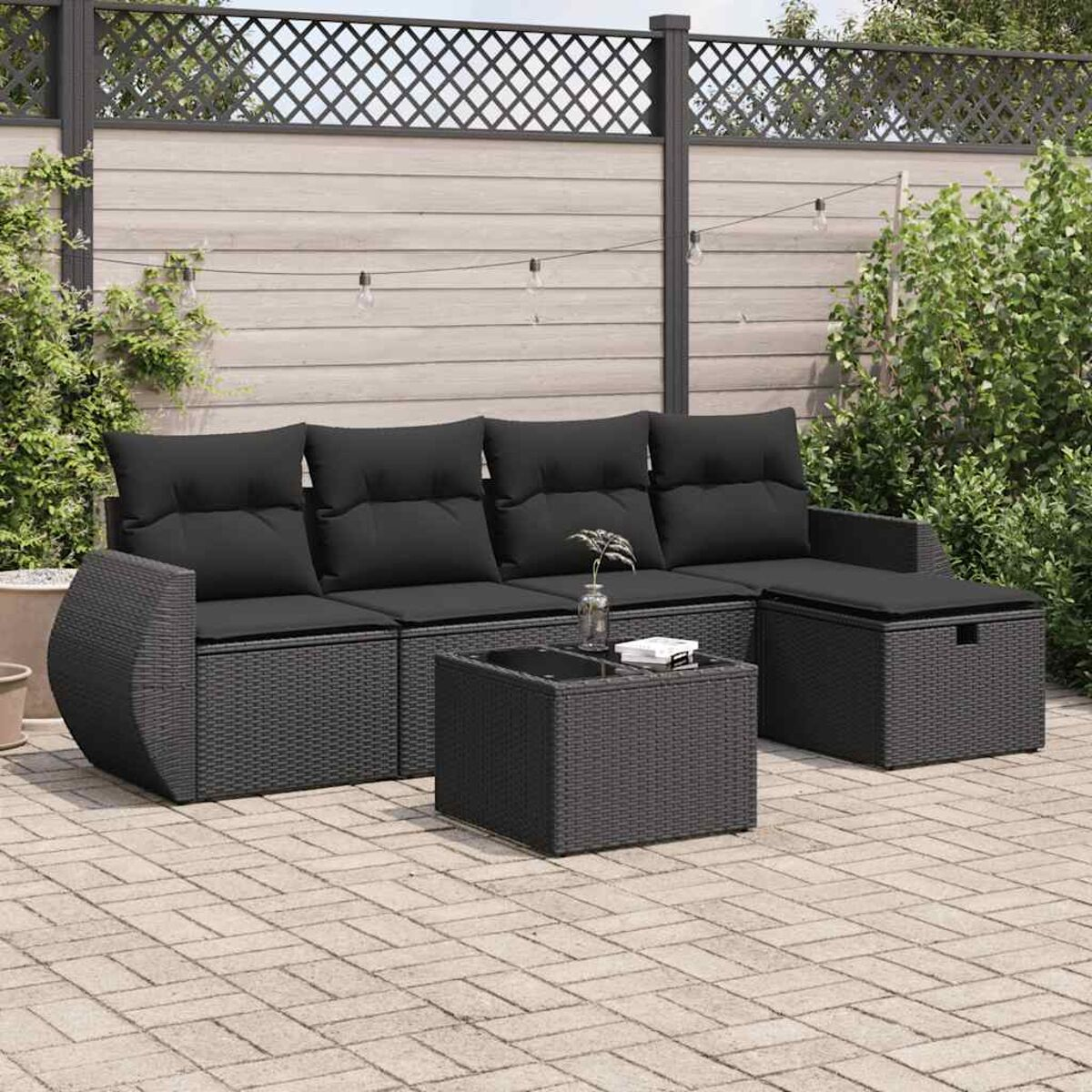 Set da patio esterno con divano, tavolino e pouf. Cuscini neri e trama intrecciata.
