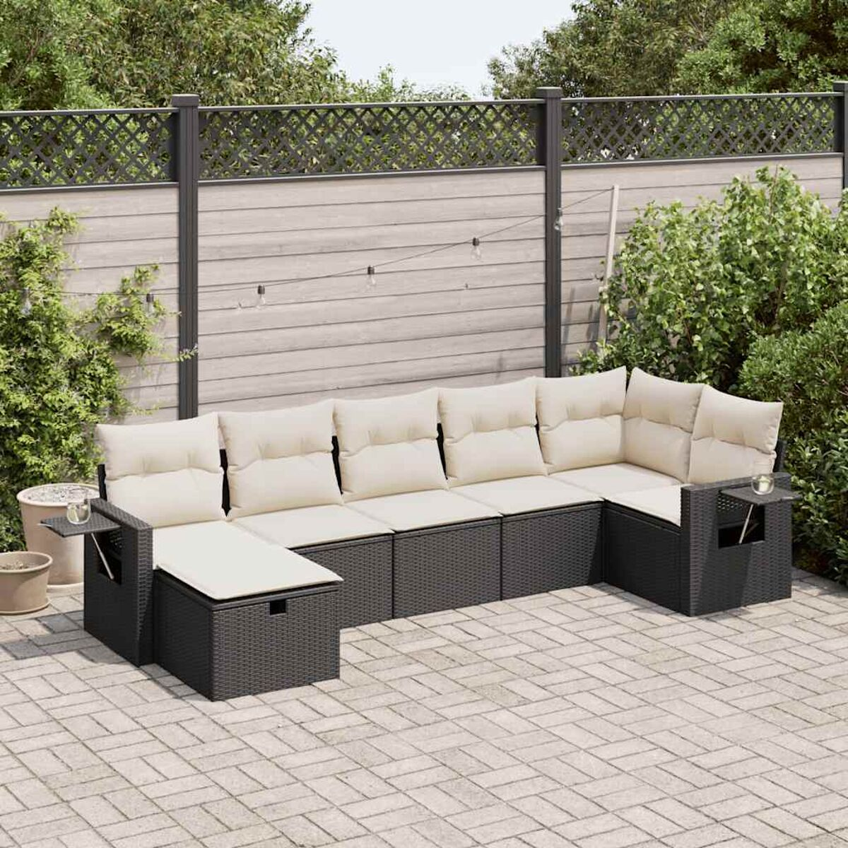 Un divano componibile grigio scuro con cuscini beige, posto su un patio con piante in vaso e una recinzione.