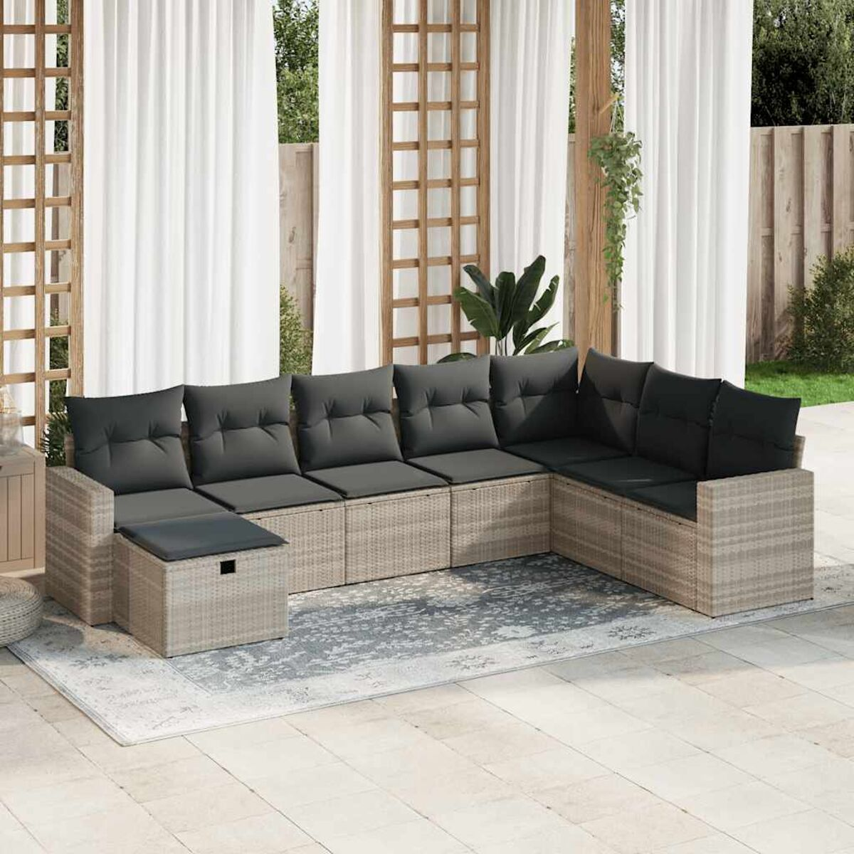 L-förmiges Rattan-Sofa mit dunkelgrauen Kissen auf einer Terrasse. Hintergrund: weiße Vorhänge und Holzbalken.