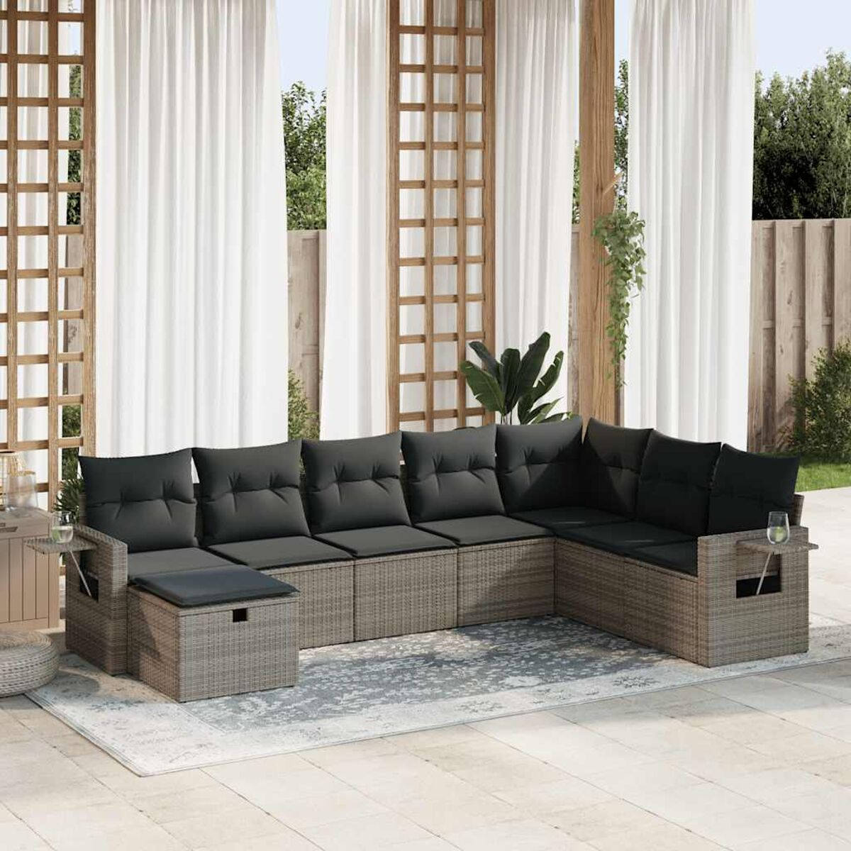 Outdoor-Wicker-Sofagarnitur. Graue Korbmöbel mit dunkelgrauen Kissen. Gardinen und Pergola im Hintergrund.