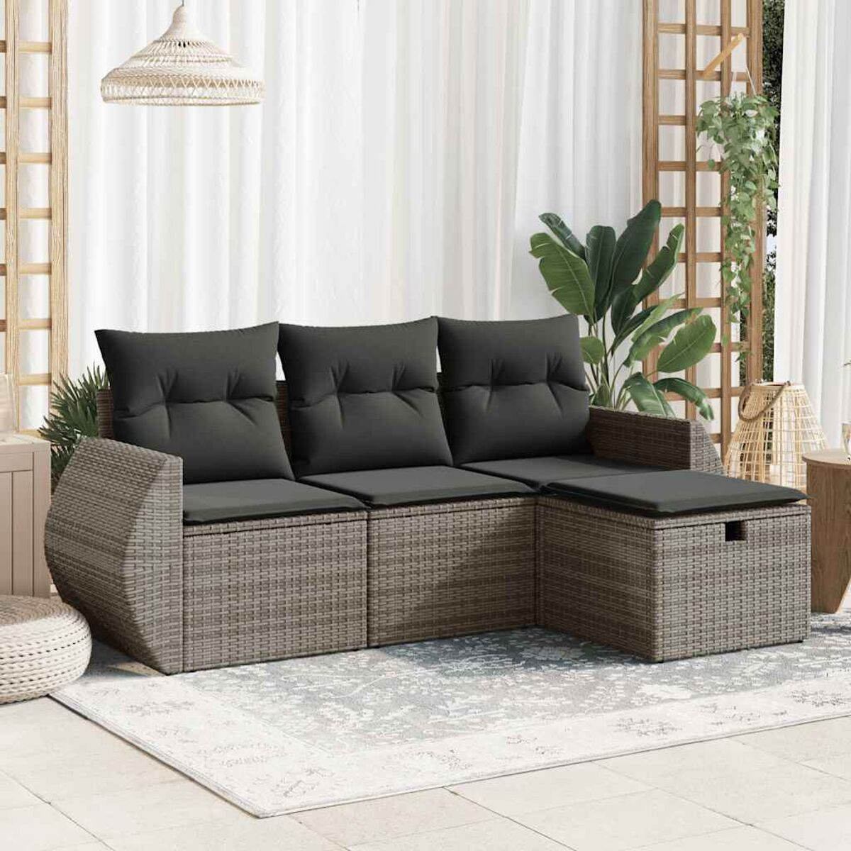 Graues Rattan-Sofa mit schwarzen Kissen auf einem Teppich, Pflanzen im Hintergrund.