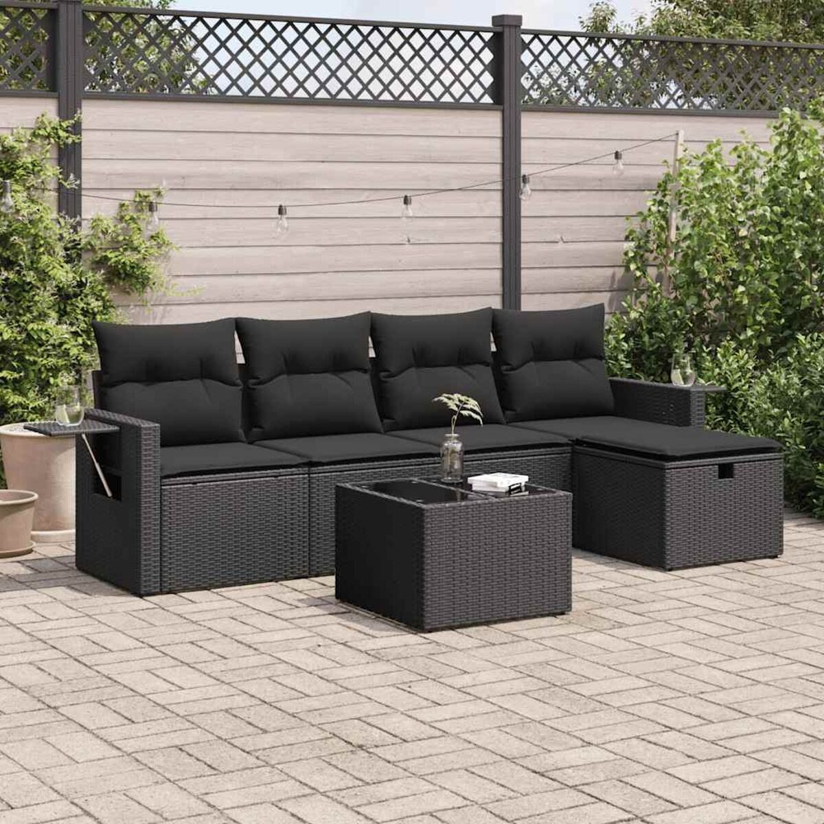 Schwarzes Outdoor-Set aus Korbgeflecht mit schwarzen Kissen. Enthält Sofa, Tisch und Ottomane. Patio im Hintergrund.