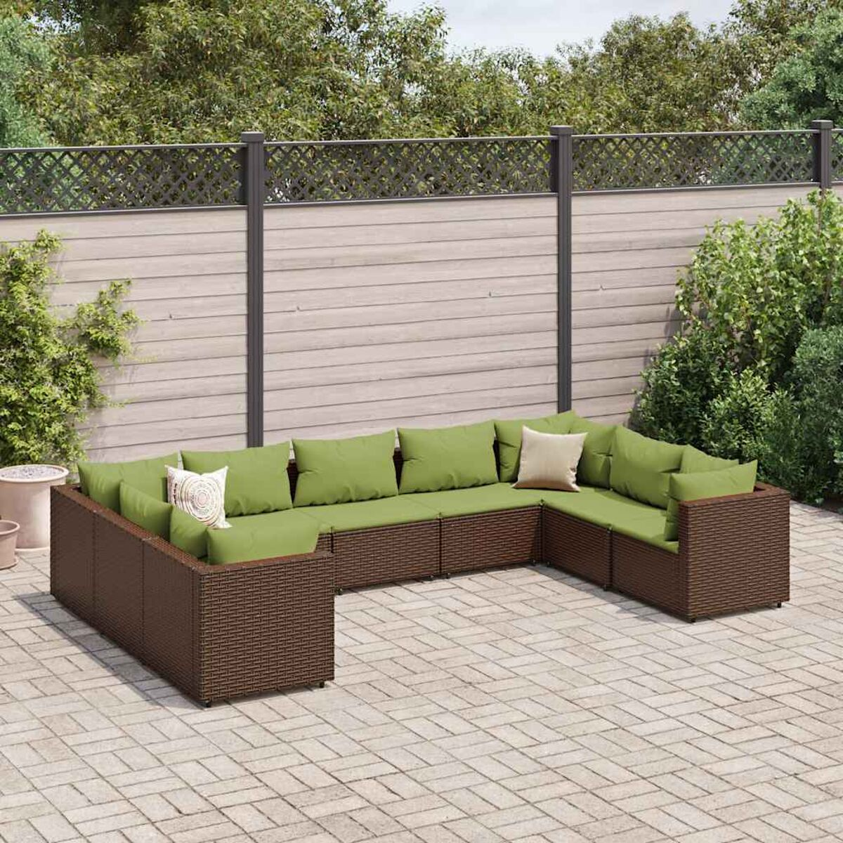 U-förmiges braunes Outdoor-Set aus Korbgeflecht mit grünen Kissen. Gegen Zaun.