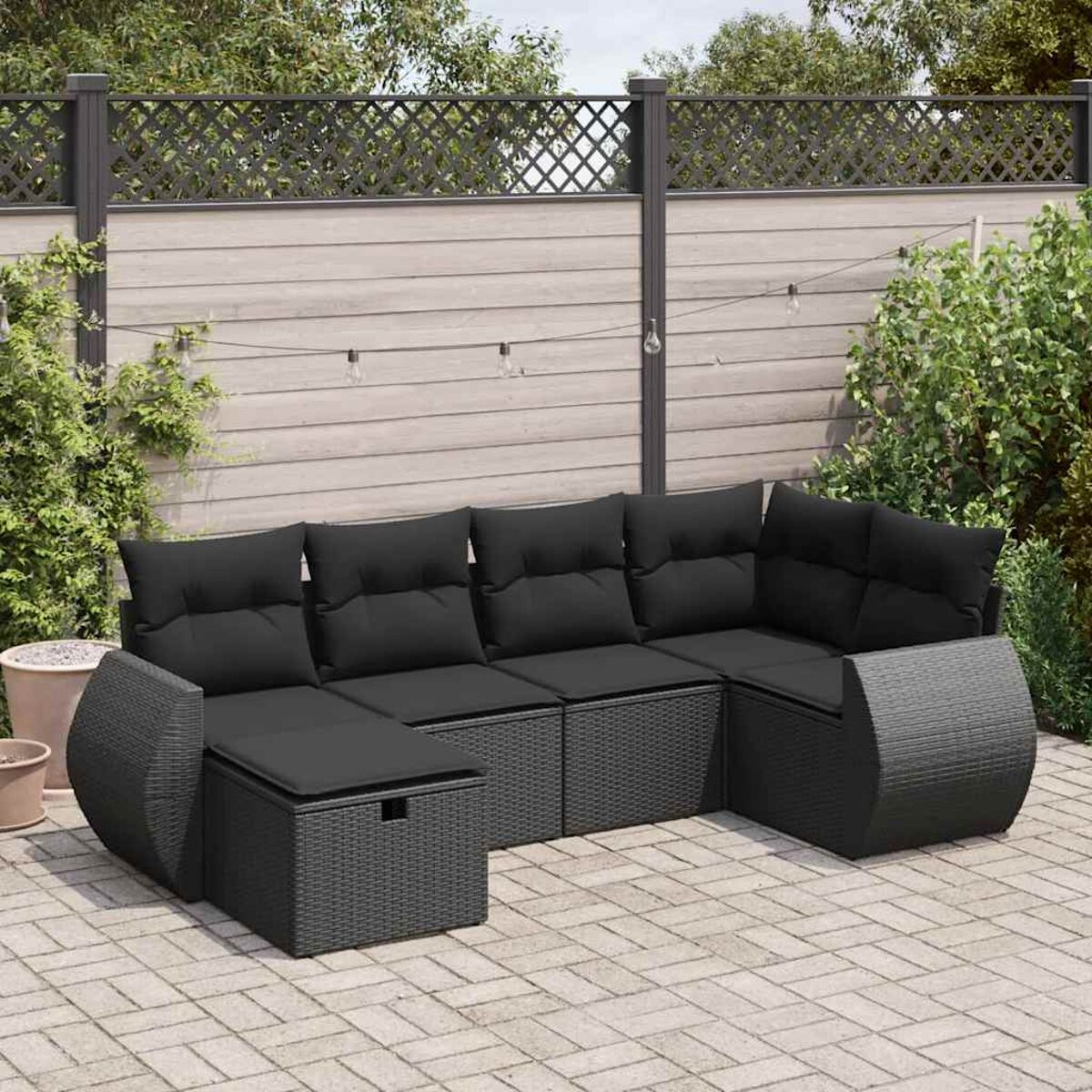 Divano componibile nero da esterno con cuscini, su un patio con verde.