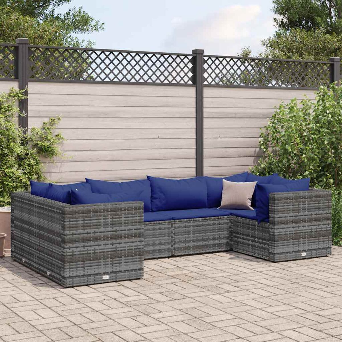 Sofá seccional de exterior de ratán gris con cojines azules en un patio de ladrillos, con valla de madera.