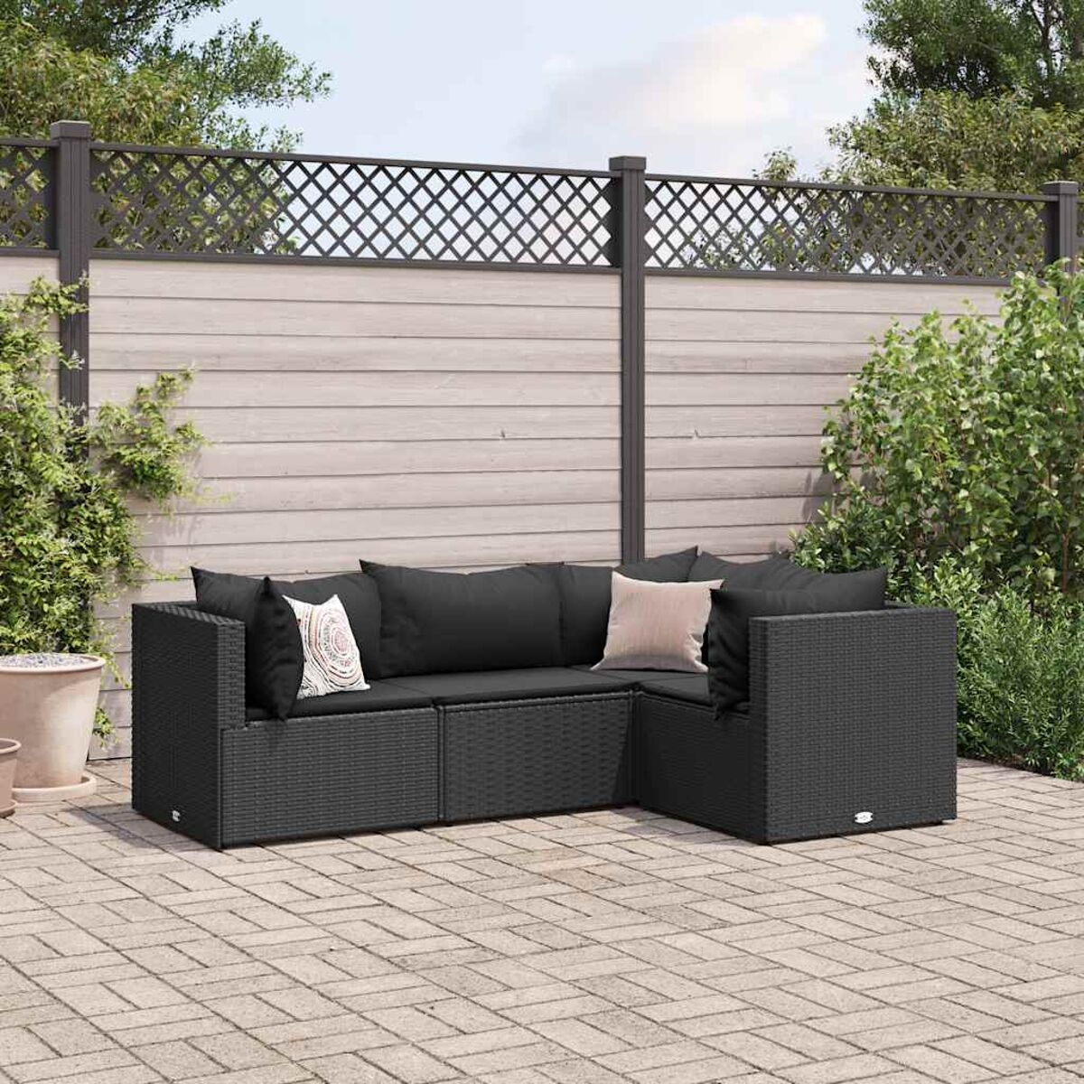 Sofá seccional exterior de mimbre negro con cojines negros, en un patio de ladrillos.