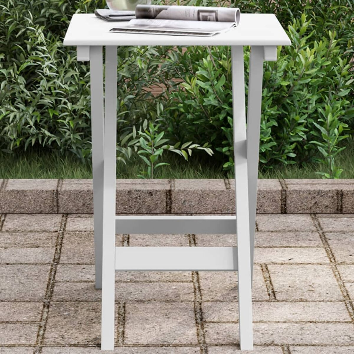 Weißer Klapptisch. Es hat eine flache Oberfläche. Eine Zeitung und ein Glas stehen auf dem Tisch.