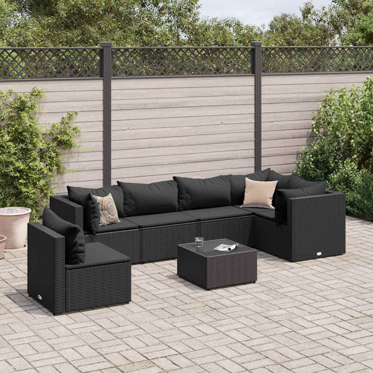 Set divano in rattan nero su un patio. Include un divano, una sedia e un tavolino.