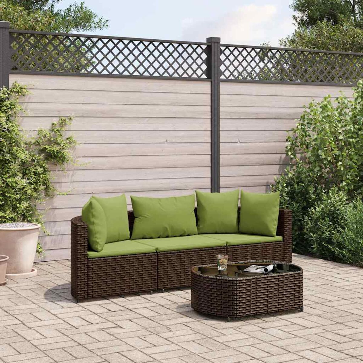 Divano in rattan marrone con cuscini verdi e tavolino in un giardino con una recinzione.