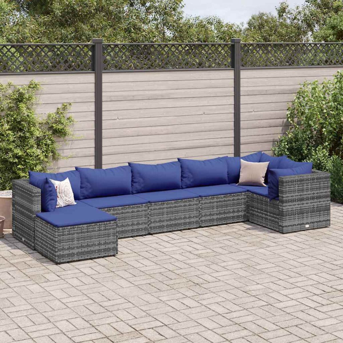 U-förmiges graues Korbsessel-Set mit blauen Kissen. Set auf Ziegelterrasse vor einem Zaun.