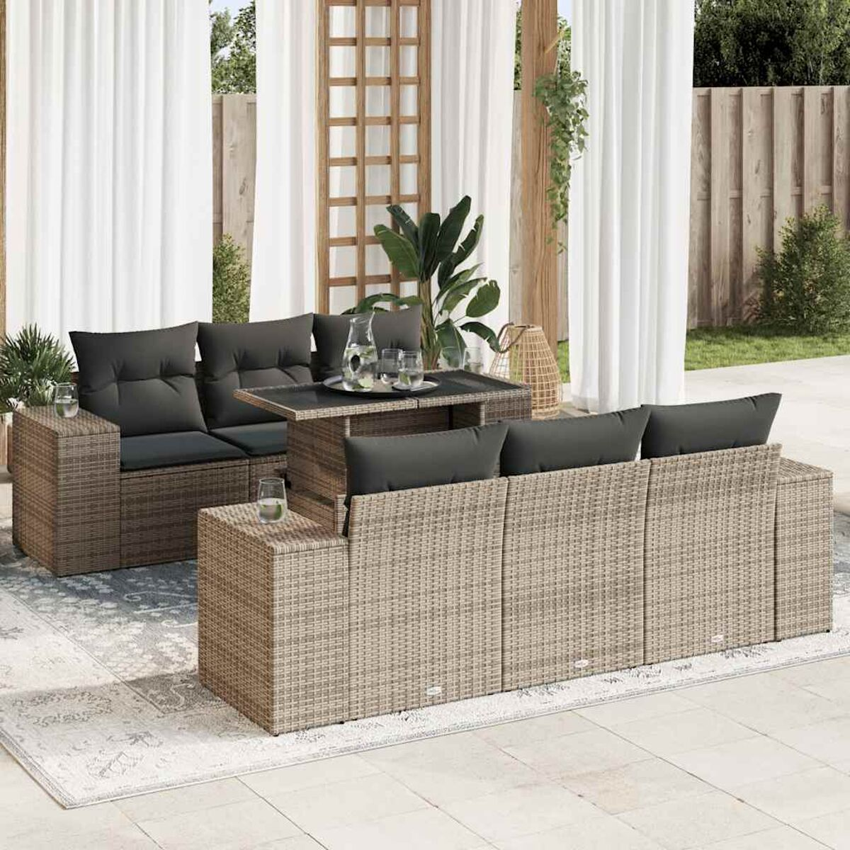 Set divano in rattan con tavolino con piano rialzabile e cuscini grigi. Ambiente esterno con tappeto.