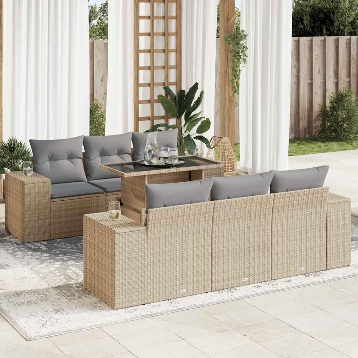 Ein Outdoor-Set aus Korbgeflecht mit grauen Kissen und einem Tisch. Weiße Vorhänge sind im Hintergrund.