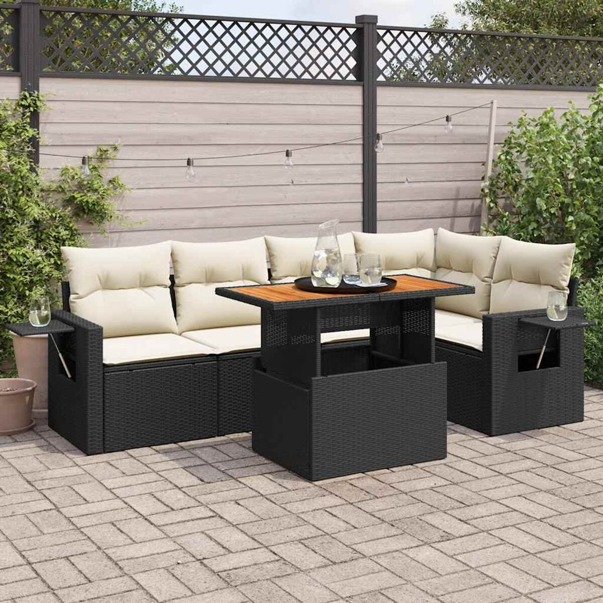 Divano componibile beige per esterni con tavolo con sollevamento su un patio pavimentato. Piante e recinzione sullo sfondo.