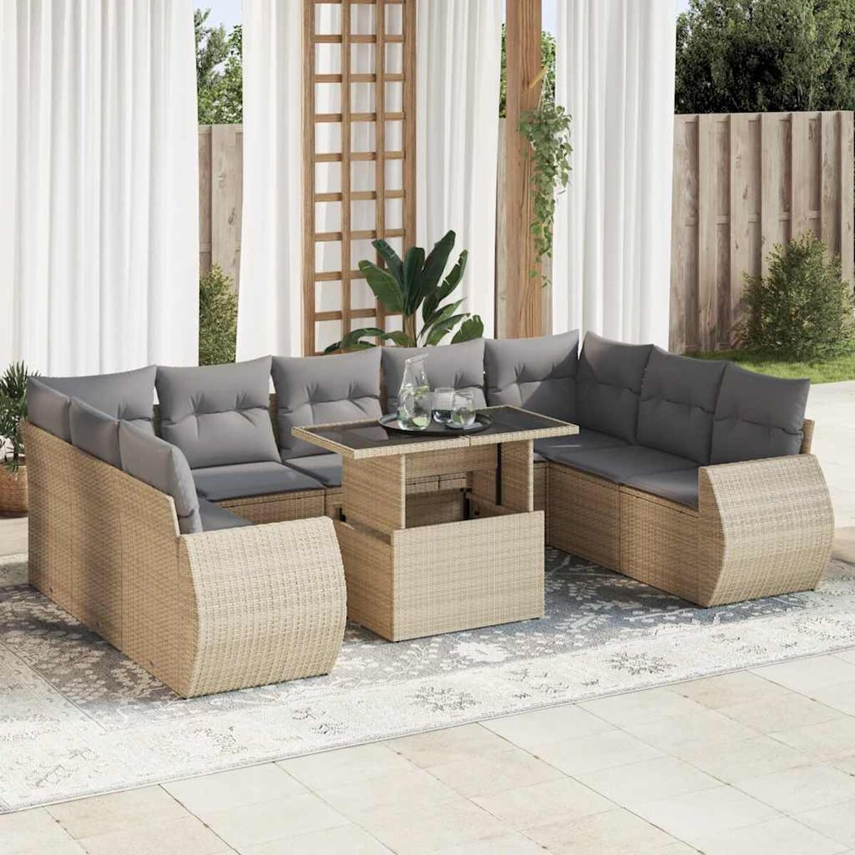 Set divani in vimini da esterno con cuscini grigi, tavolo e tappeto su un patio, con tende e piante.