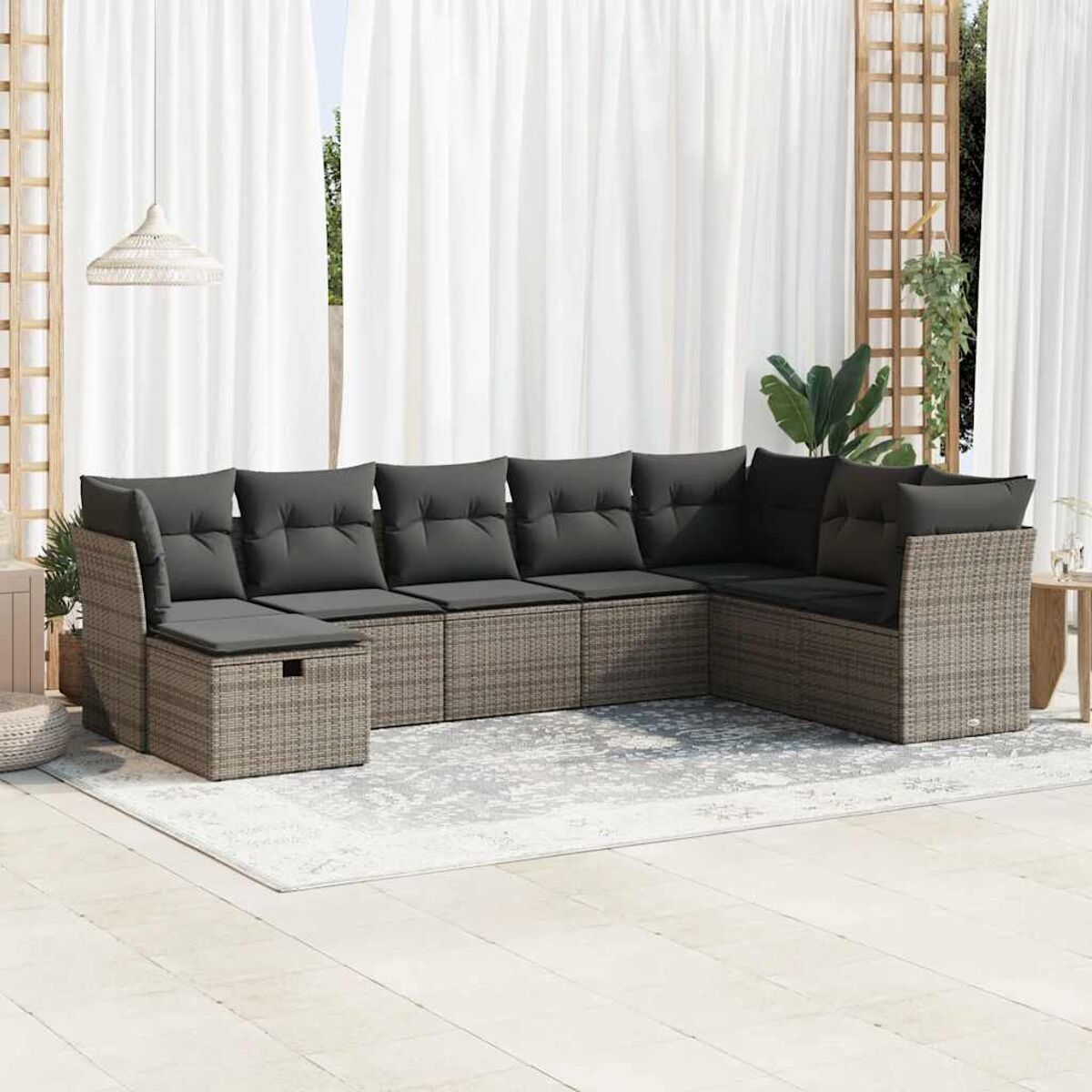 Beiges Rattan-Ecksofa mit dunkelgrauen Kissen. Hintergrund: weißer Teppich, Vorhänge und ein Spalier.