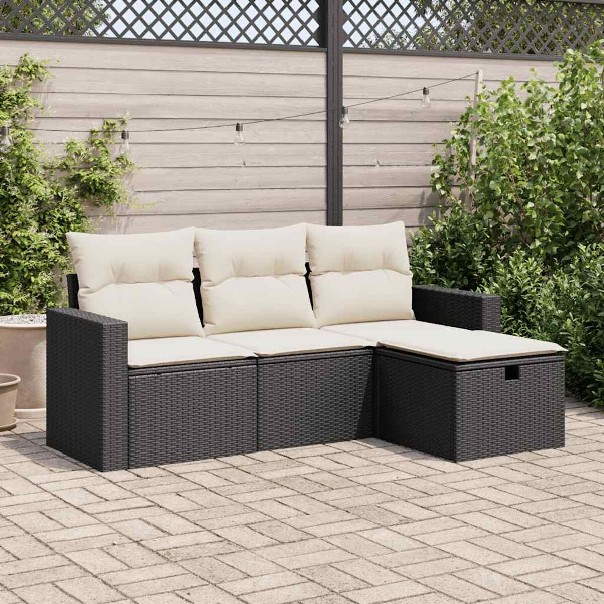 Schwarzes Rattan-Sofa mit weißen Kissen, auf Pflastersteinen platziert.