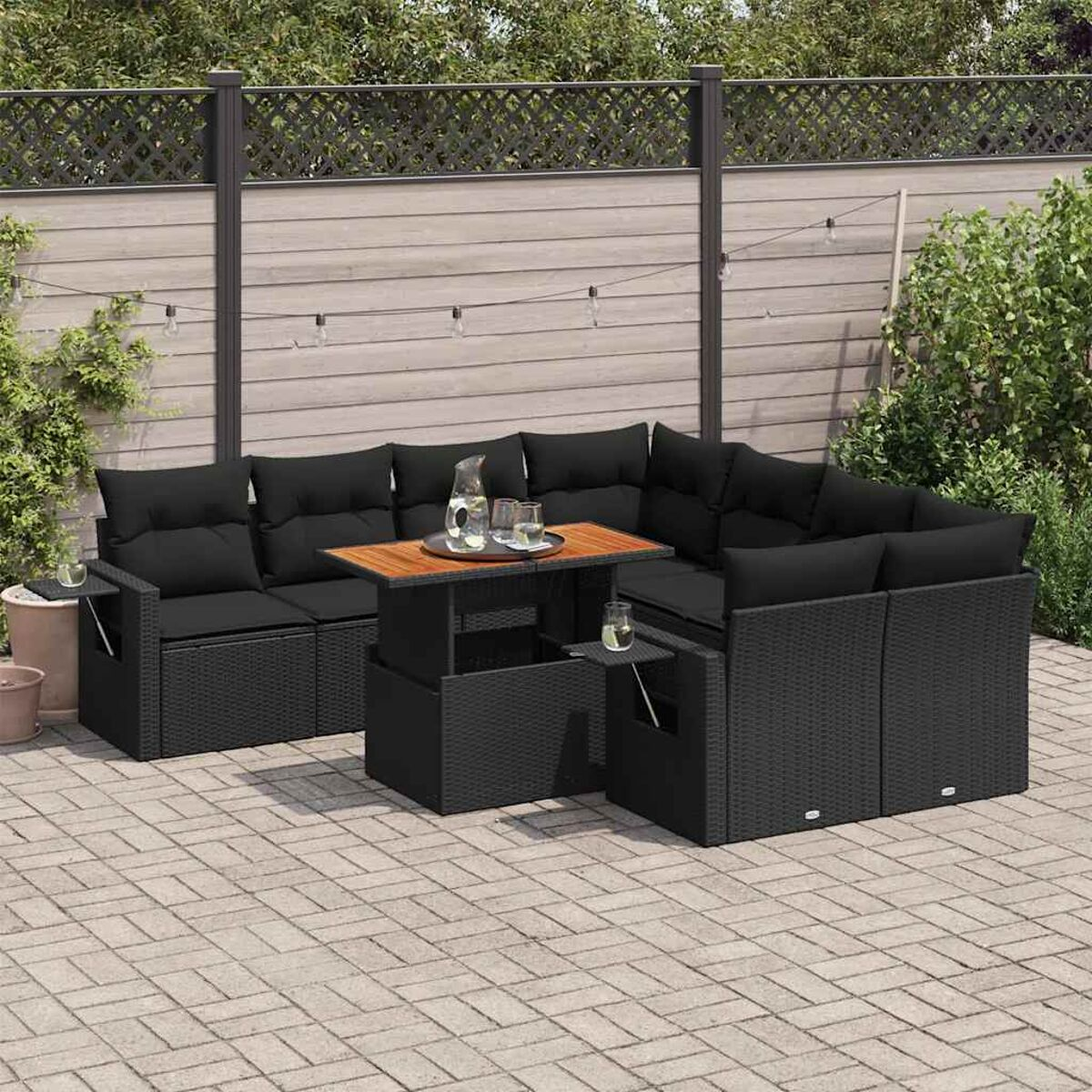 Set divano da esterno in rattan nero con cuscini neri e tavolo in legno su un patio.