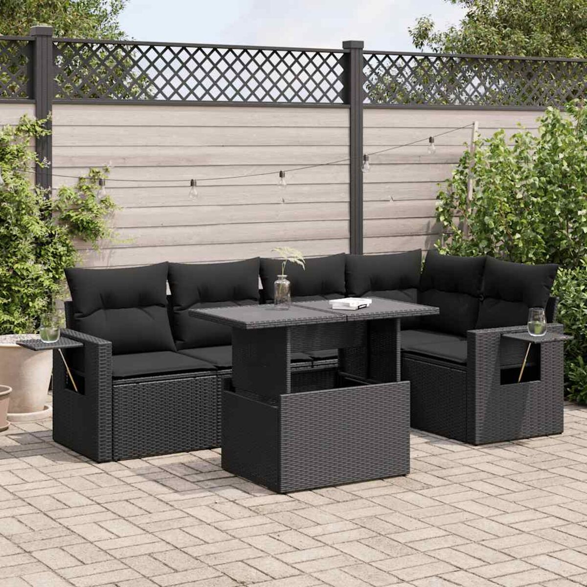Set di sedute da esterno in rattan nero con tavolo, divani e tavolini su un patio in mattoni.