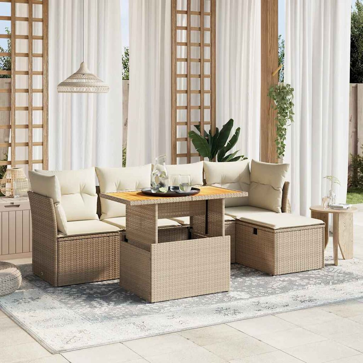 Set divano rattan da esterno con cuscini beige e un tavolo centrale. Tende bianche sullo sfondo.