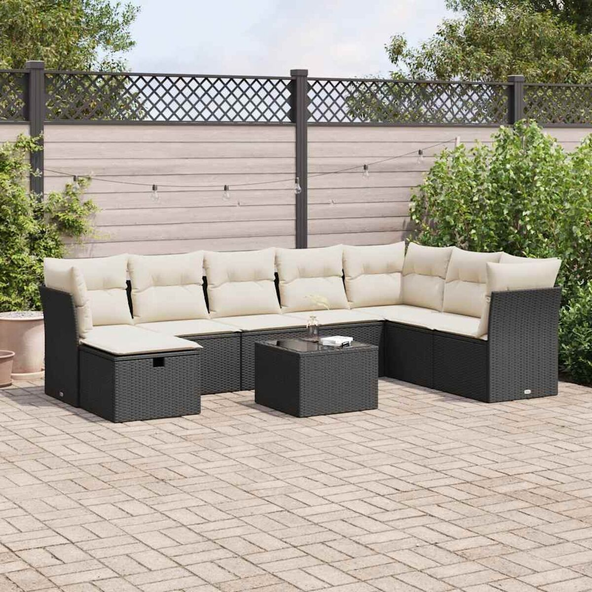 Schwarzes Outdoor-Ecksofa mit kleinem Tisch auf einer Backstein-Terrasse, Zaun im Hintergrund.