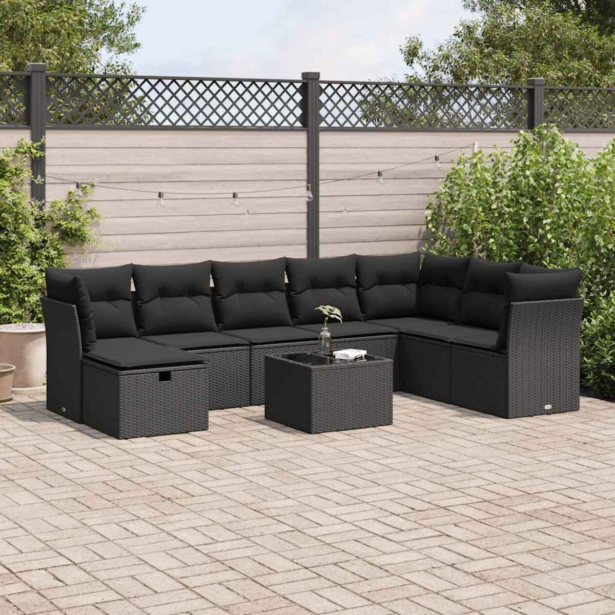 Divano componibile da esterno in rattan nero con cuscini neri. Tavolino quadrato. Patio in pavé.