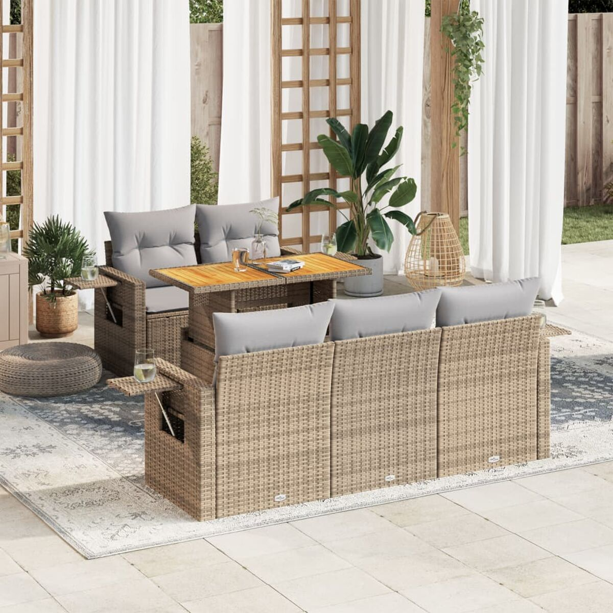 Rattan-Sofa-Set im Freien mit Kissen, Holztisch, Pflanzen und weißen Vorhängen.