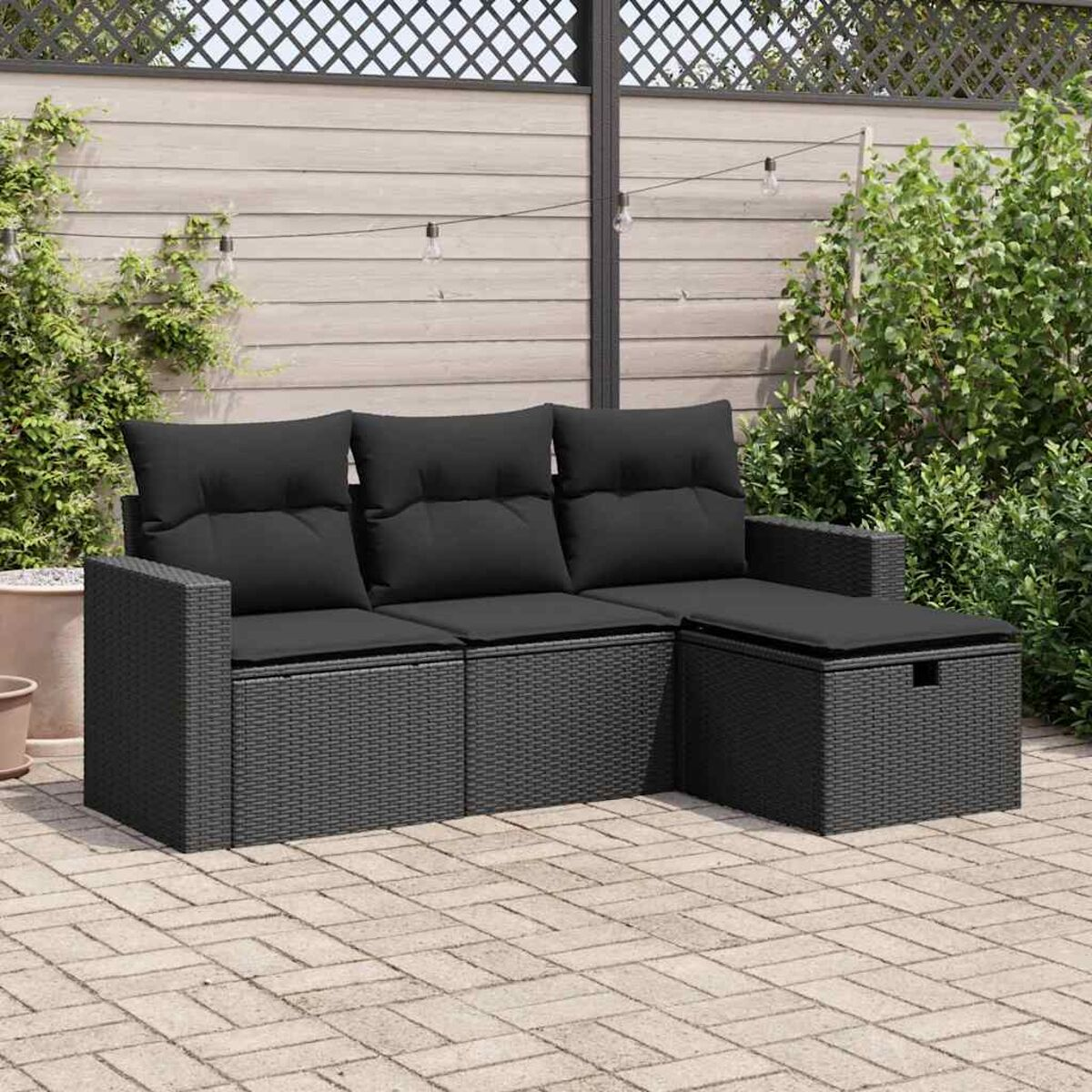 Un divano in vimini nero con un cuscino nero su un patio. Lo sfondo è un giardino.