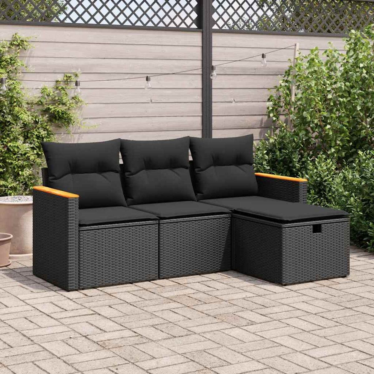 Seccional exterior de mimbre negro con cojines negros. El conjunto tiene apoyabrazos de madera. Valla de madera detrás.