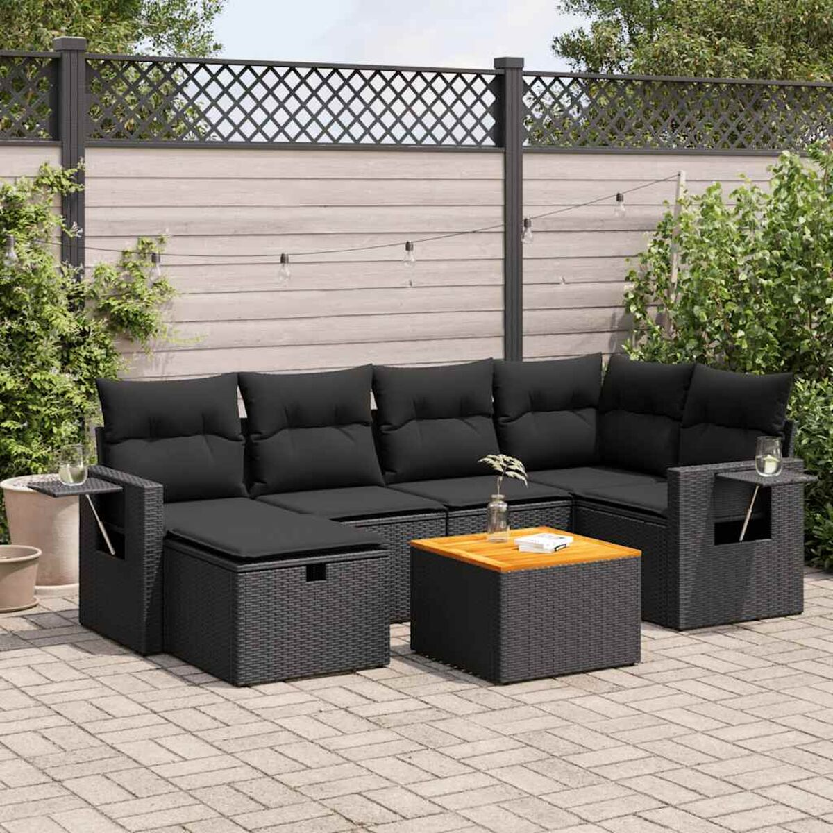 Set di sedute da esterno con design intrecciato nero. Include divano, pouf e tavolo su un'area pavimentata.